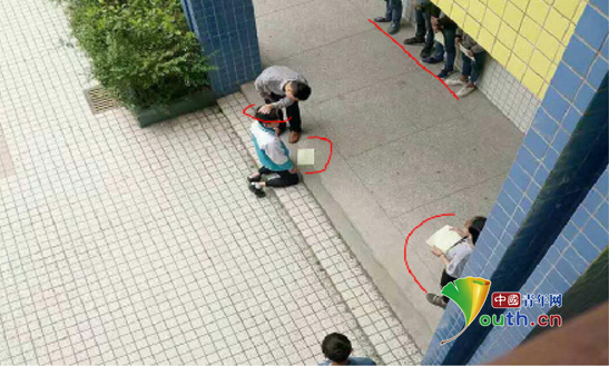 图片显示，张姓老师揪住跪在地上的学生的头发，学生面前还有一排学生靠墙站着，侧面也有学生站着。